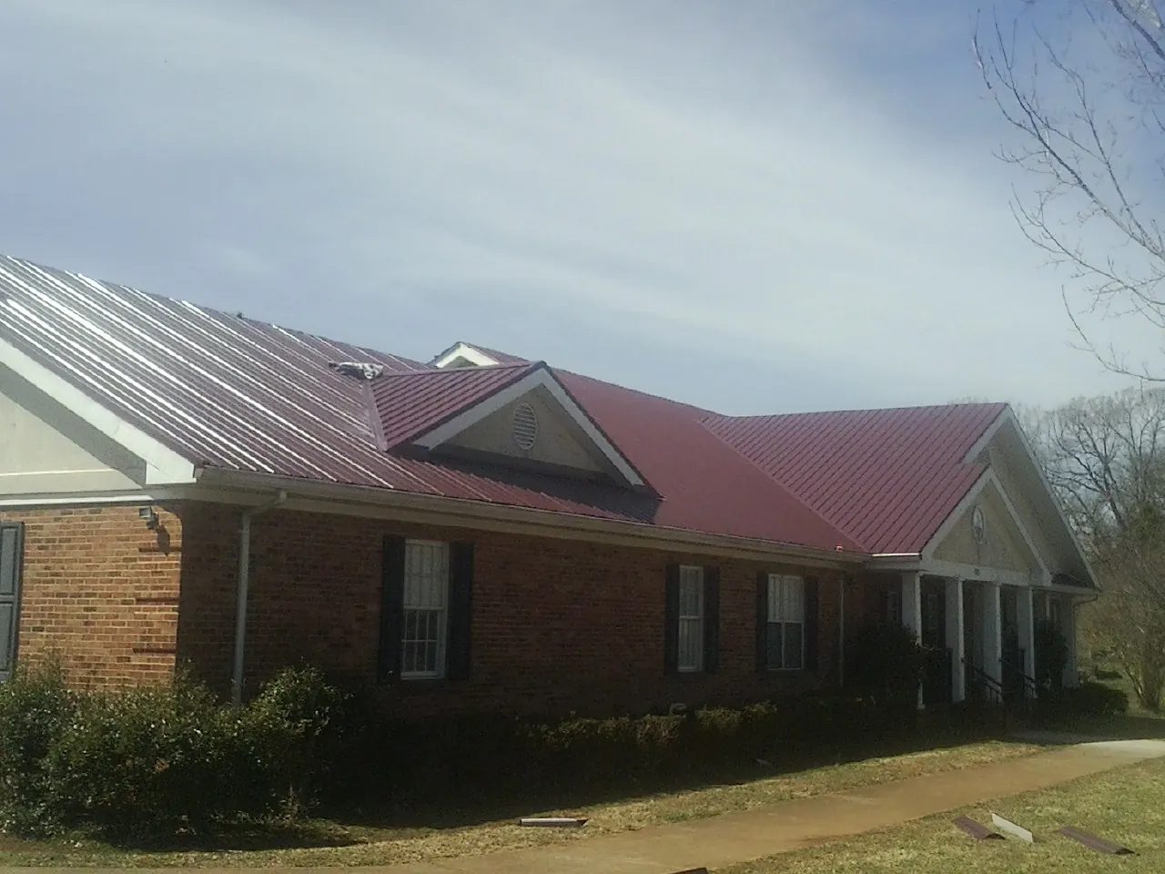 Red metal roof with gabled entries on a long brick building, from a Hail Damage Roof Repair job in Grand Island