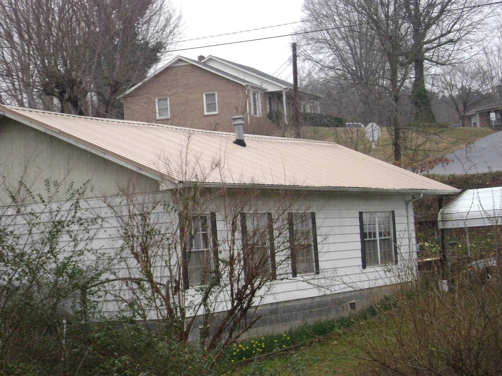 Tan metal roof on a white sided house set into a hillside — Commercial Roofing by Roofing Brothers in Grand Island